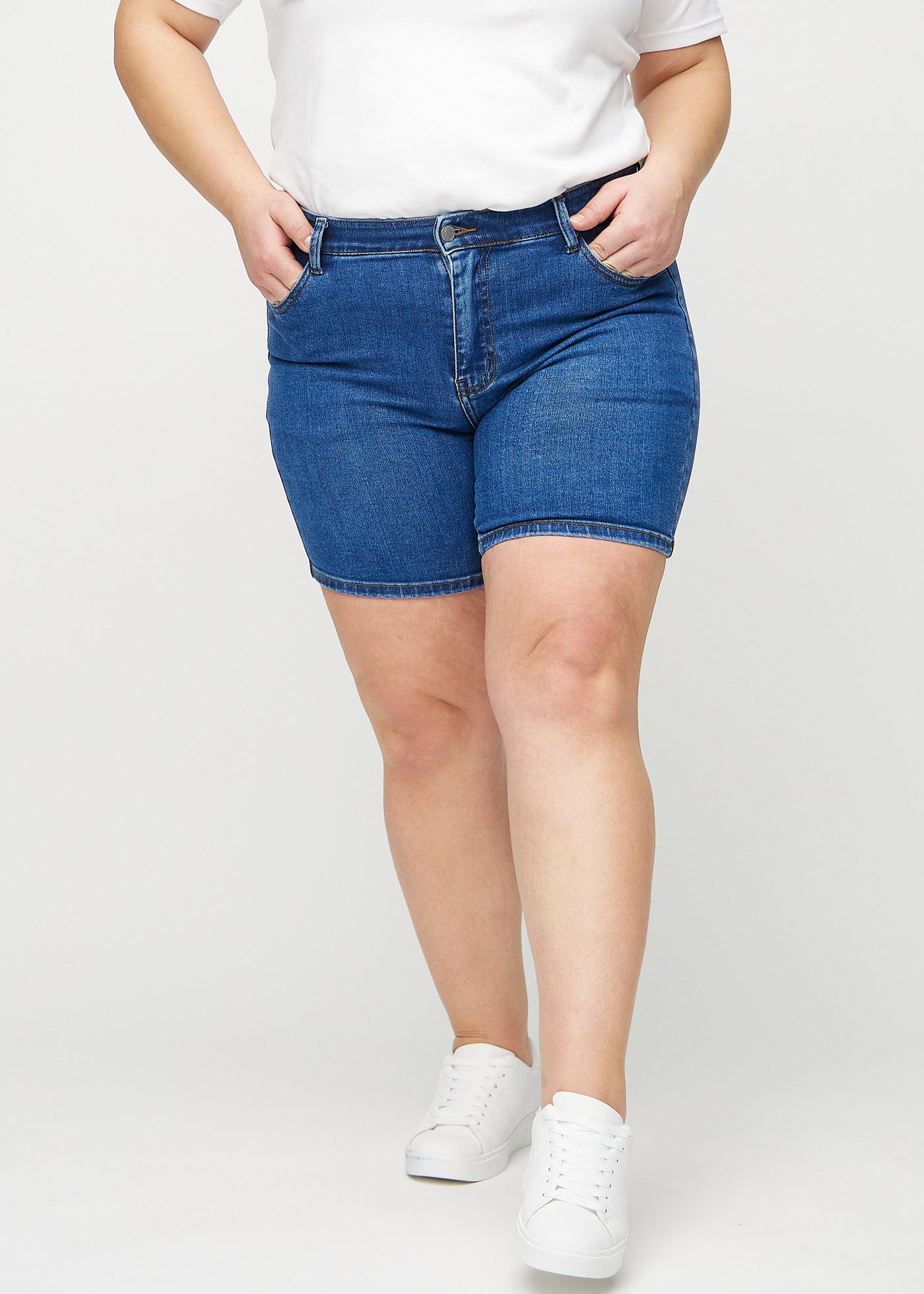 Mørk denim skinny short shorts, modelnavn Oceans, som sidder tæt til, og slutter midt på låret på en plus-size model, set forfra.