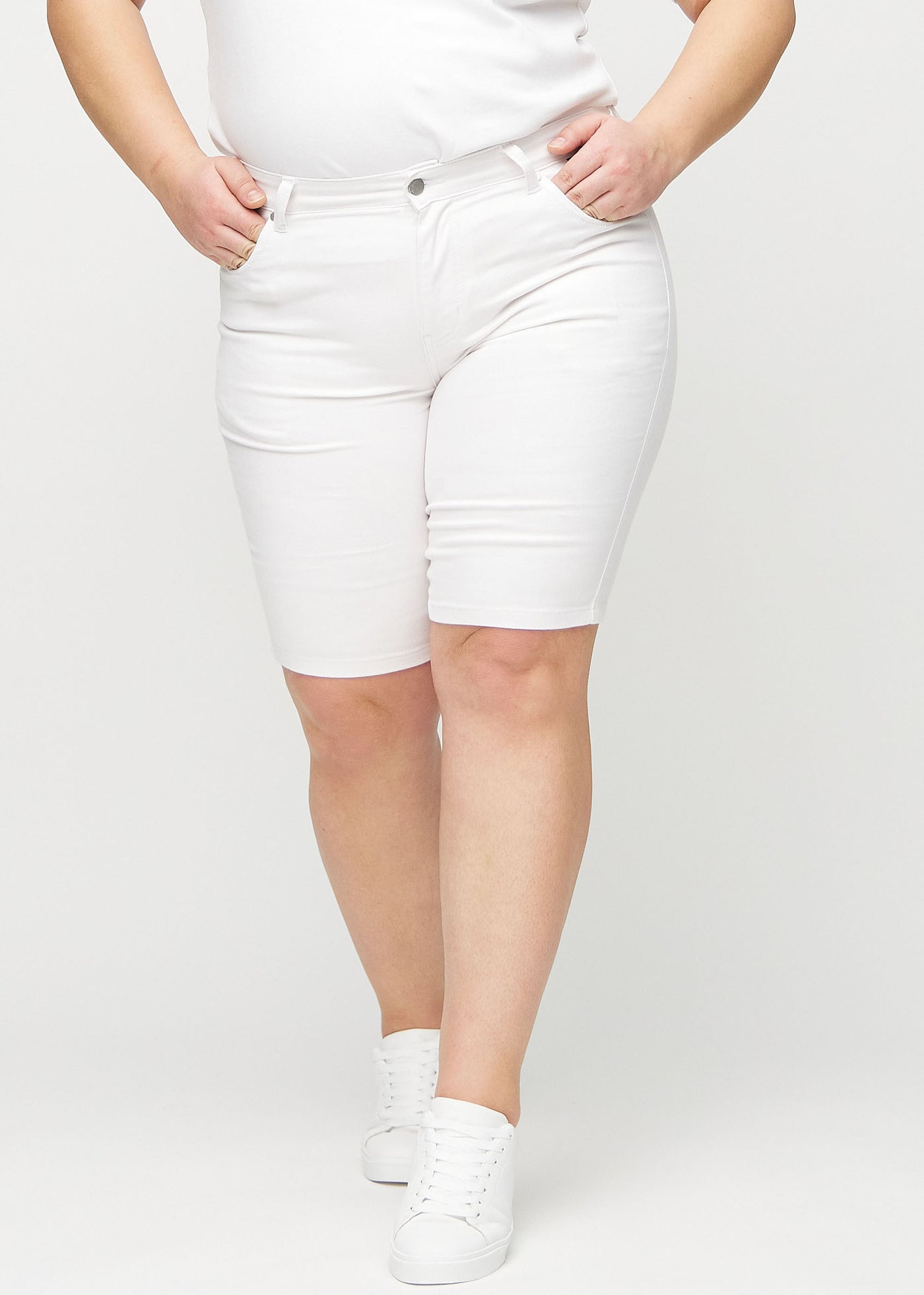 Hvide skinny middle shorts, modelnavn Marguerites, som sidder tæt til låret og slutter lige over knæet på en plus-size model, set forfra.