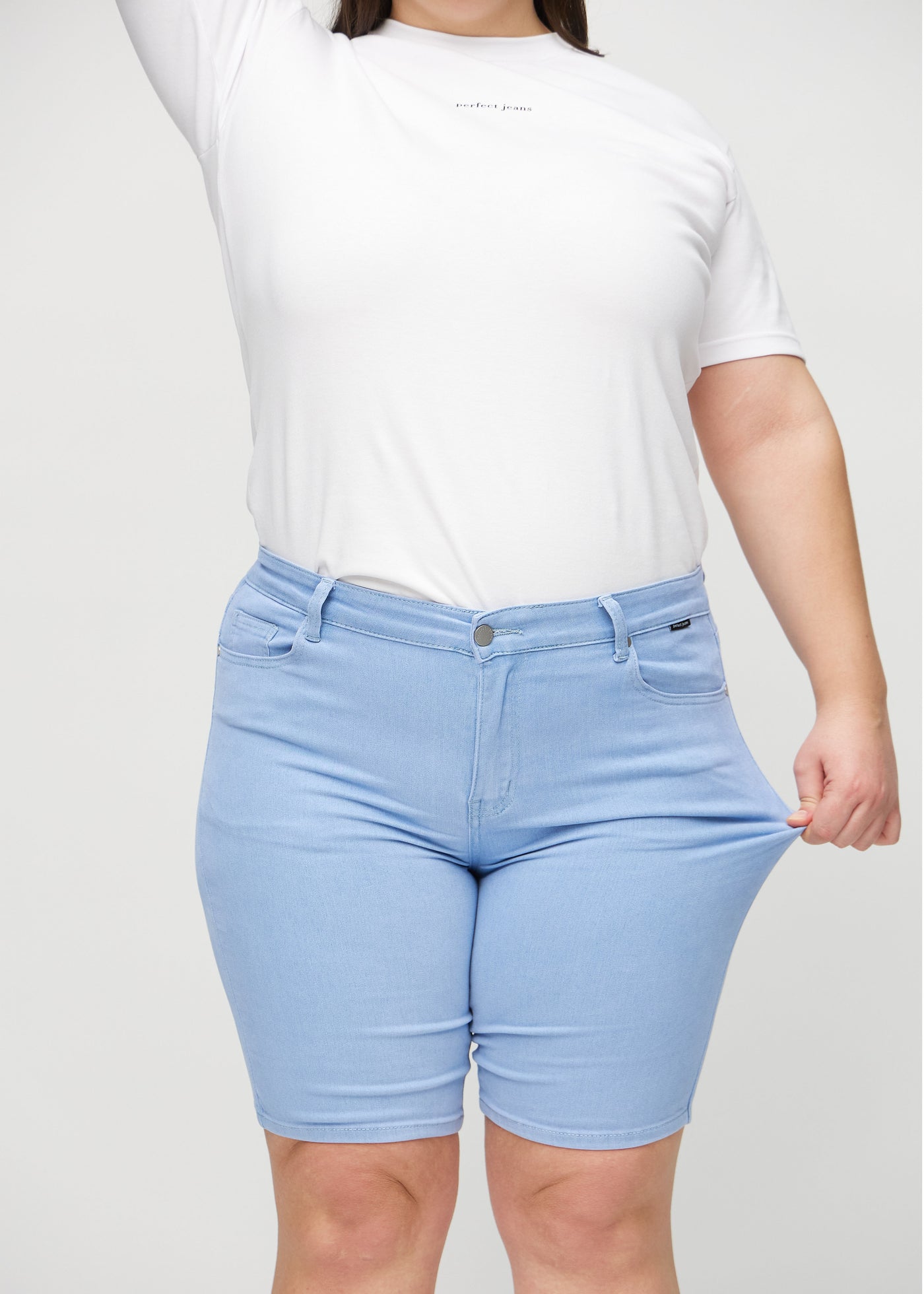 Plus-size model strækker shortsene ved låret for at vise stretch.