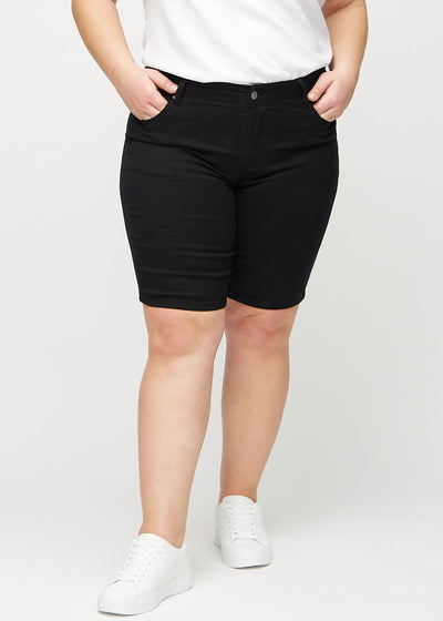 Sorte skinny middle shorts, modelnavn Ravens, som sidder tæt til låret og slutter lige over knæet på en plus-size model, set forfra.