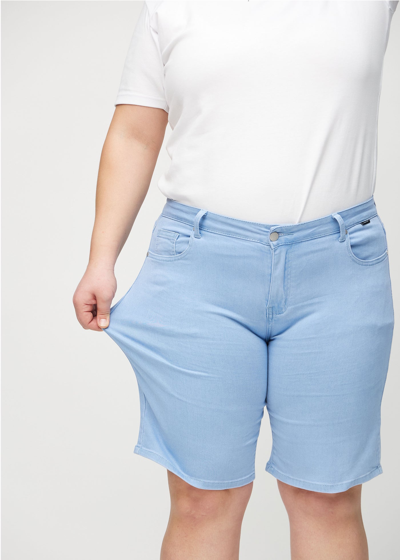 Plus-size model strækker shortsene ved låret for at vise stretch.