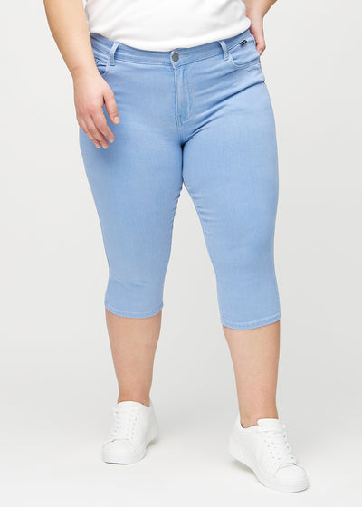 Lyseblå skinny capris, modelnavn Skies, som sidder tæt til benet og slutter lige under knæet på en plus-size model, set forfra.