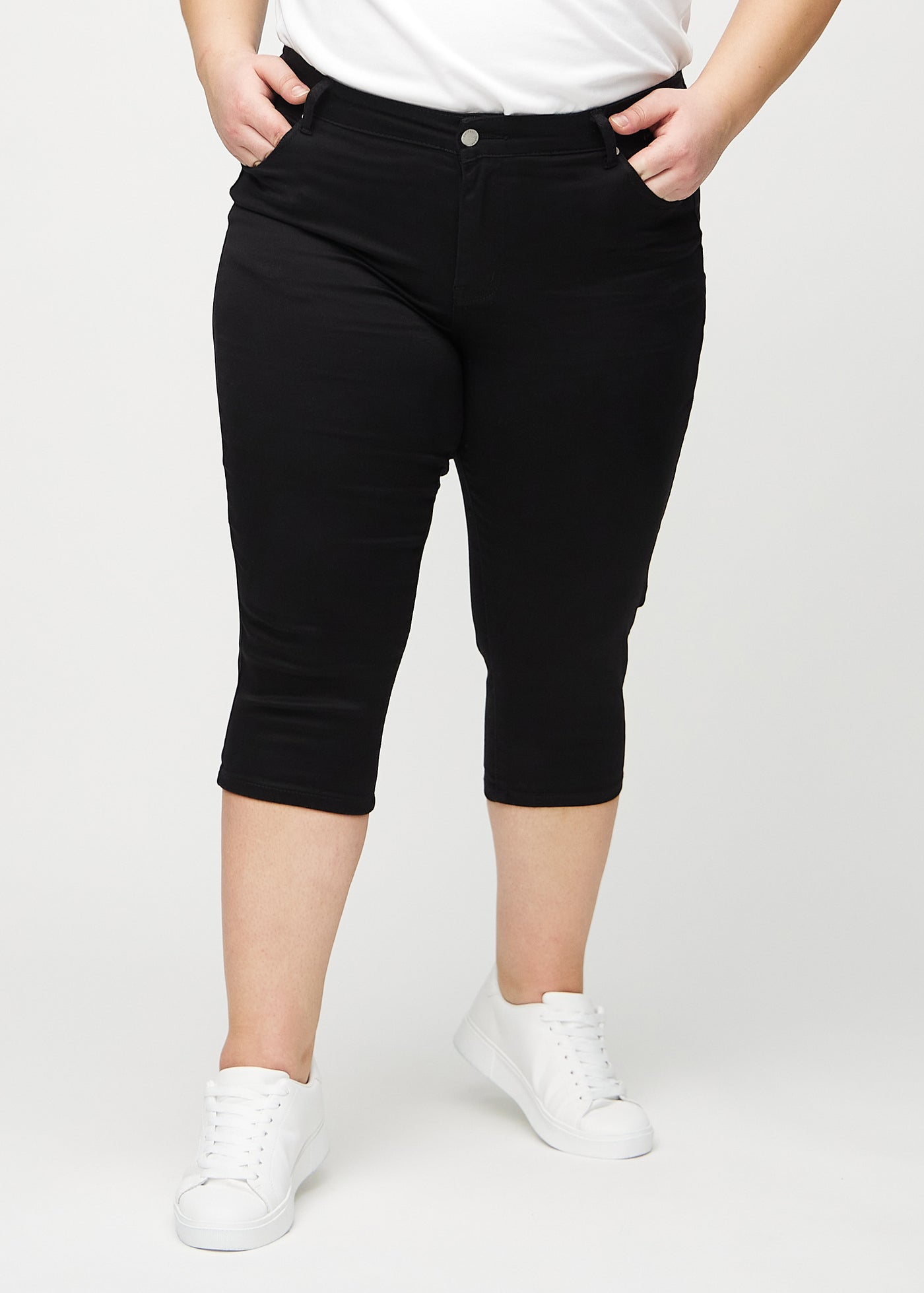 Sorte skinny capris, modelnavn Ravens, som sidder tæt til benet og slutter lige under knæet på en plus-size model, set forfra.