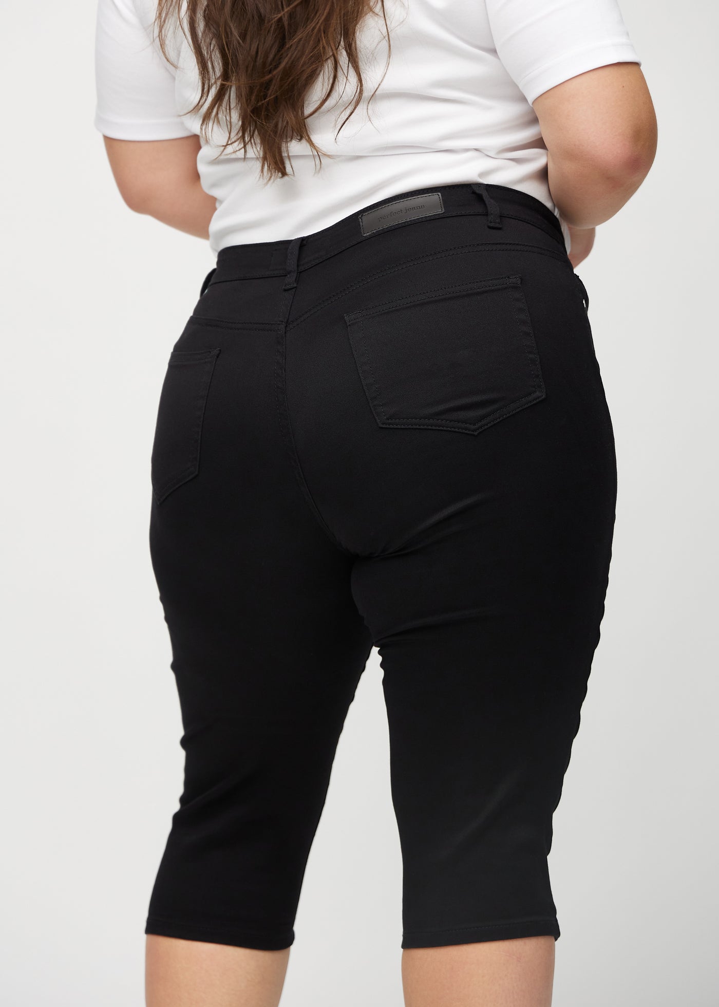 Sorte skinny capris set bagfra tæt på en plus-size model for at vise detaljer.