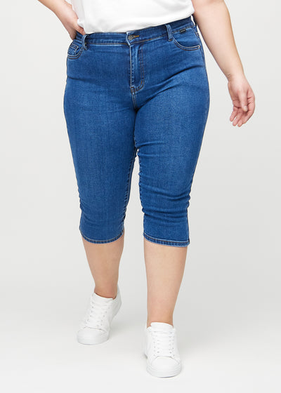 Mørk denim skinny capris, modelnavn Oceans, som sidder tæt til benet og slutter lige under knæet på en plus-size model, set forfra.