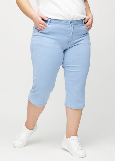 Lyseblå regular capris, modelnavn Skies, som sidder lige til benet og slutter lige under knæet på en plus-size model, set forfra.