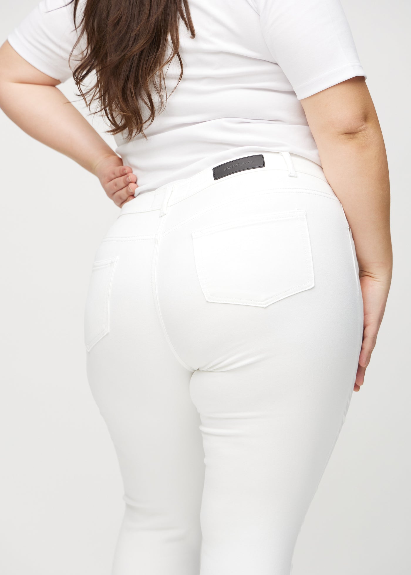 Hvide skinny jeans set bagfra tæt på en plus-size model for at vise detaljer.