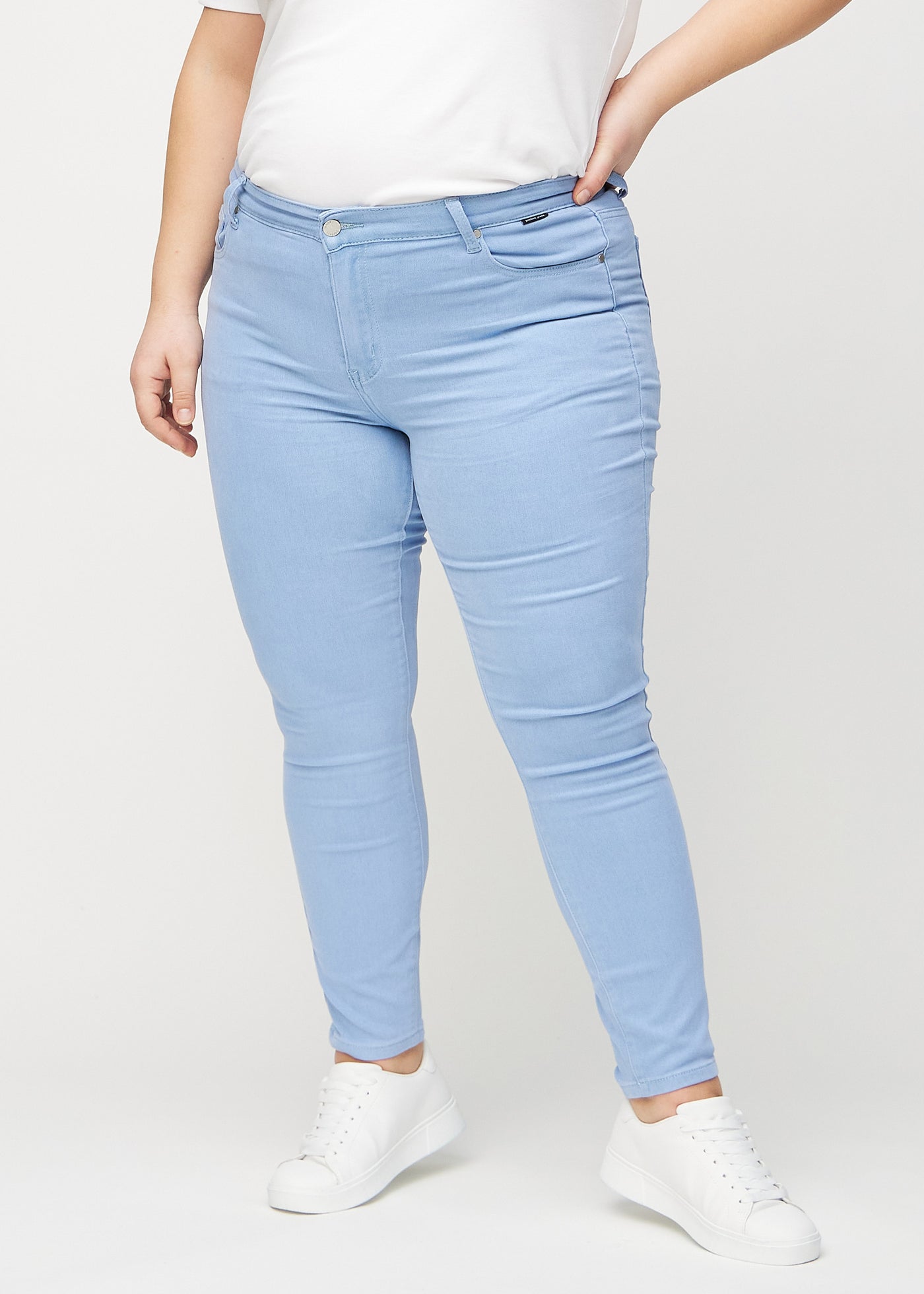 Lyseblå skinny jeans, modelnavn Skies, som sidder tæt til benet på en plus-size model, set forfra.