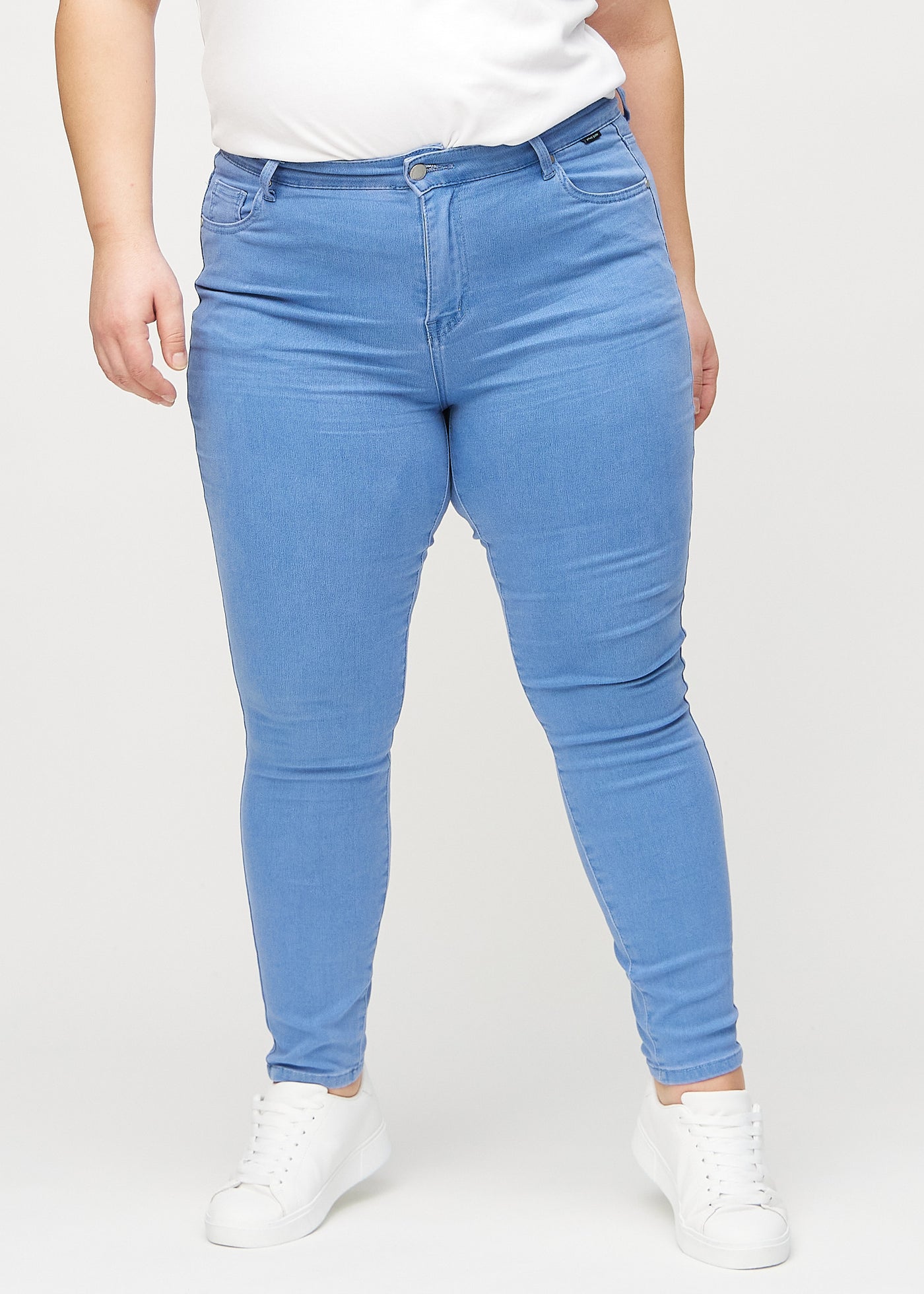 Blå skinny jeans, modelnavn Geraniums, som sidder tæt til benet på en plus-size model, set forfra.