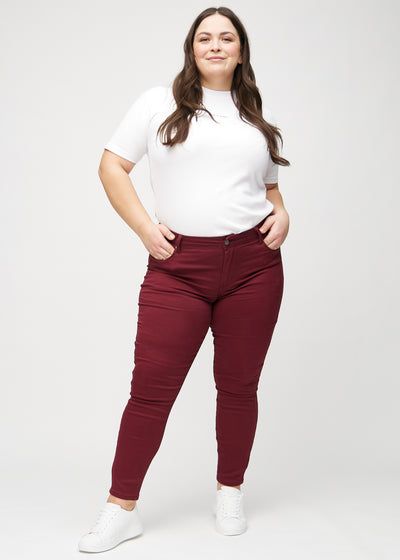 Mørkerøde skinny jeans, modelnavn Santas, som sidder tæt til benet på en plus-size model, set forfra.