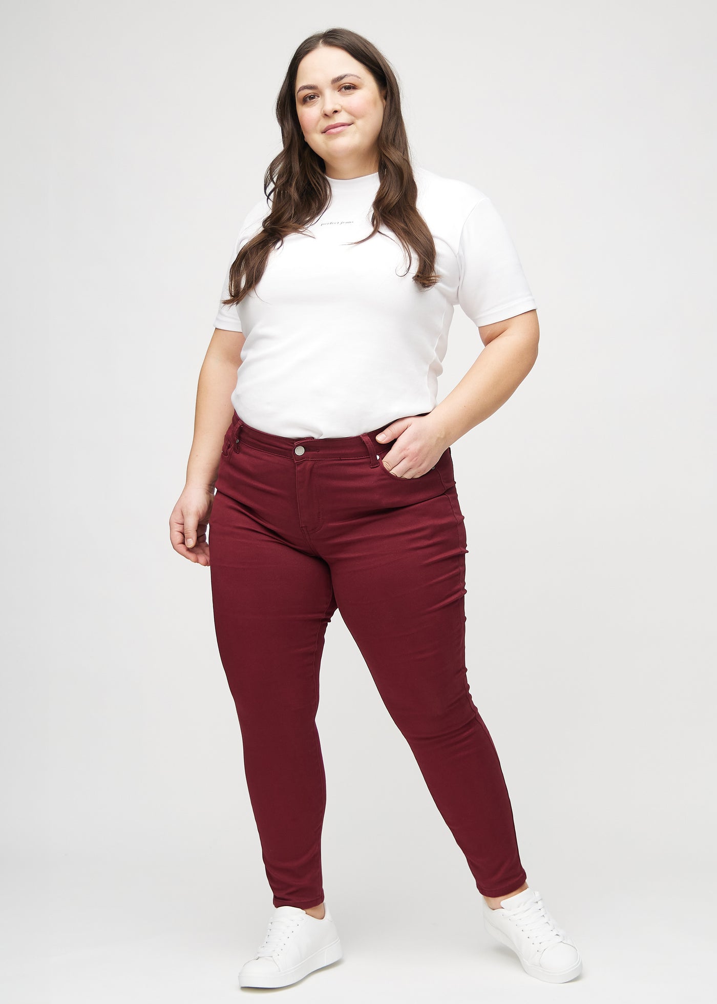 Fuldt billede af en plus-size model i mørkerøde skinny jeans.