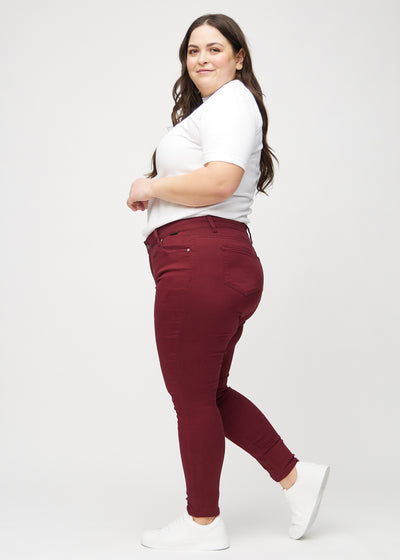 Mørkerøde skinny jeans set fra siden på en plus-size model.