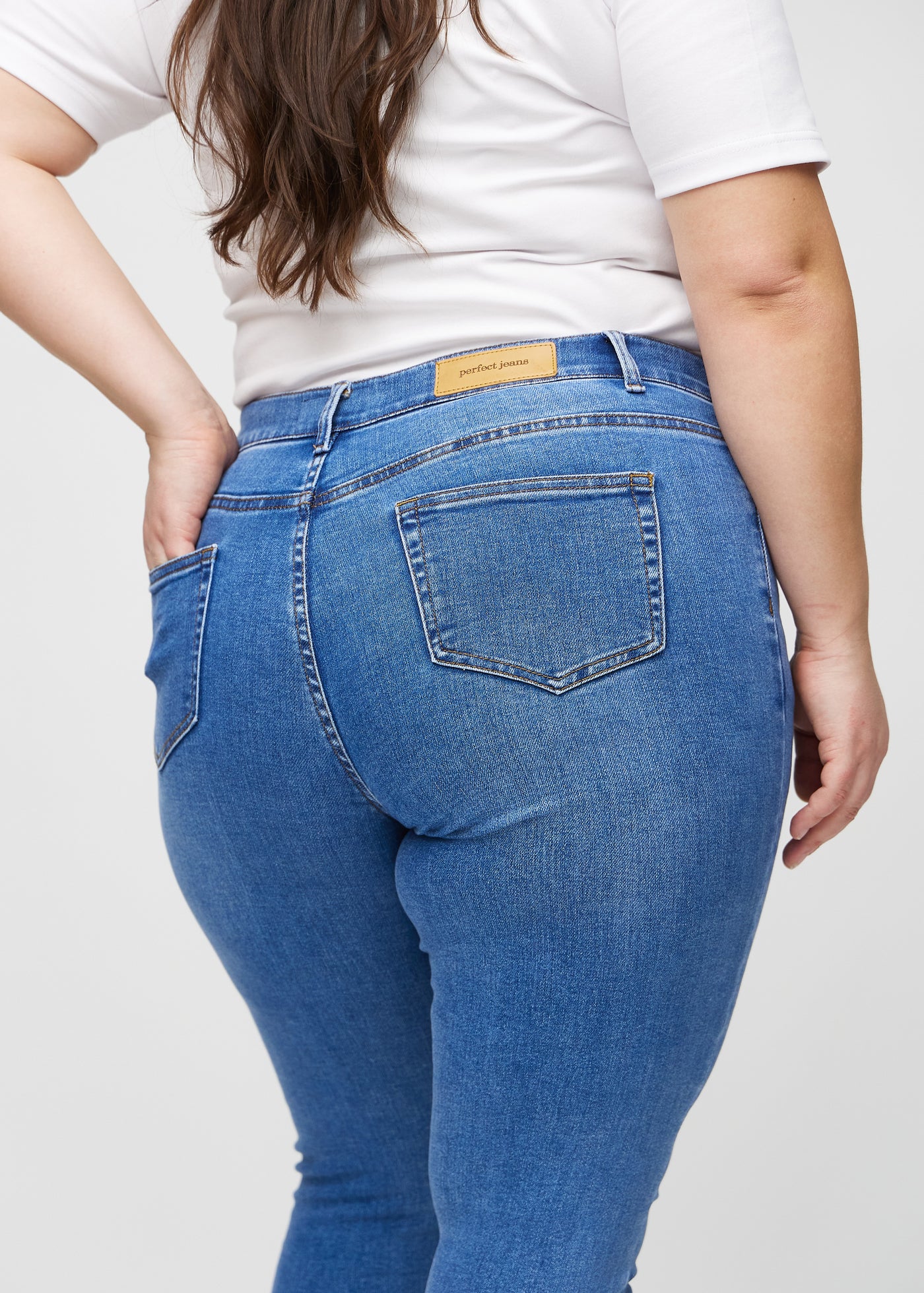 Denim skinny jeans set bagfra tæt på en plus-size model for at vise detaljer.