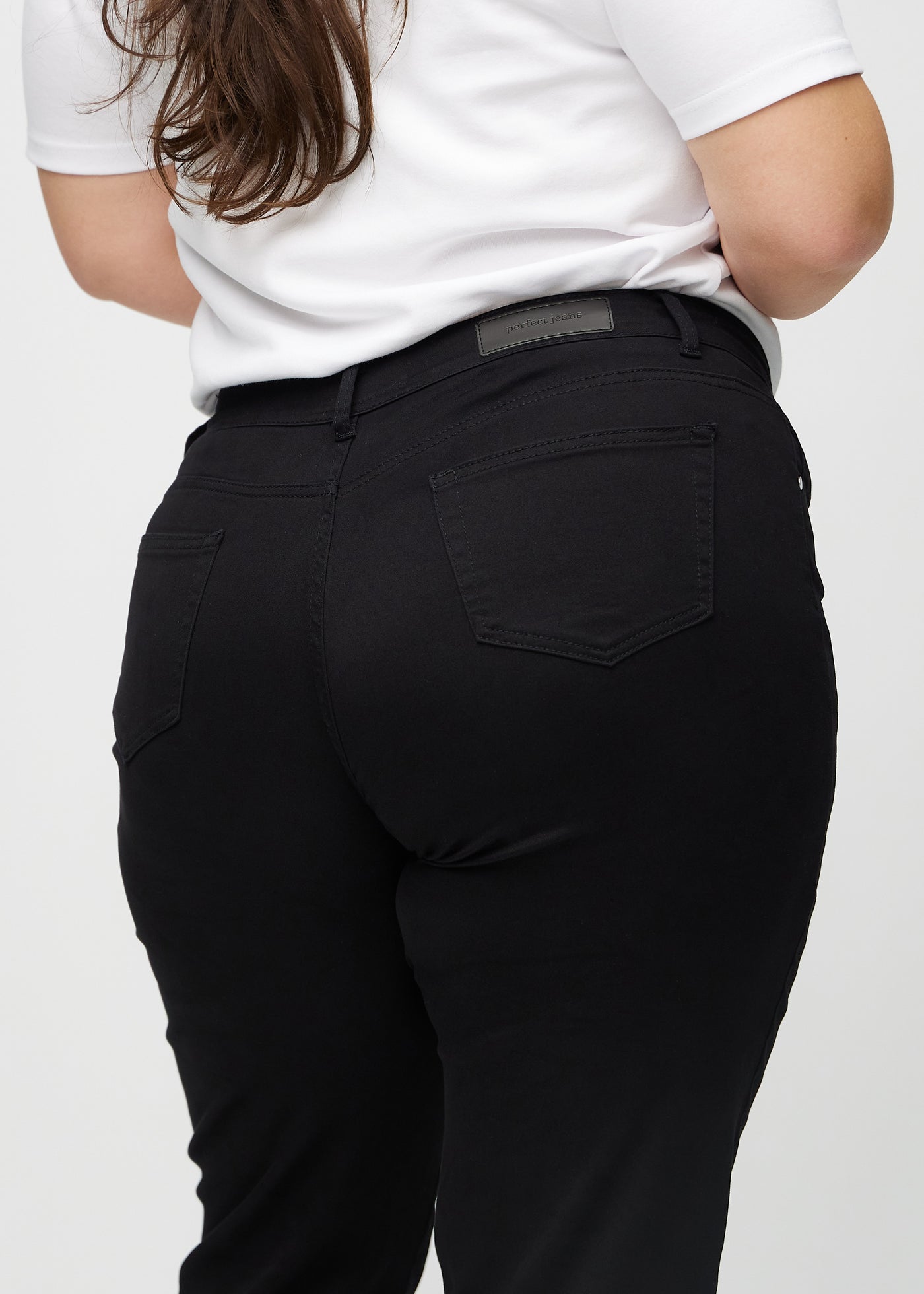 Sorte regular jeans set bagfra tæt på en plus-size model for at vise detaljer.