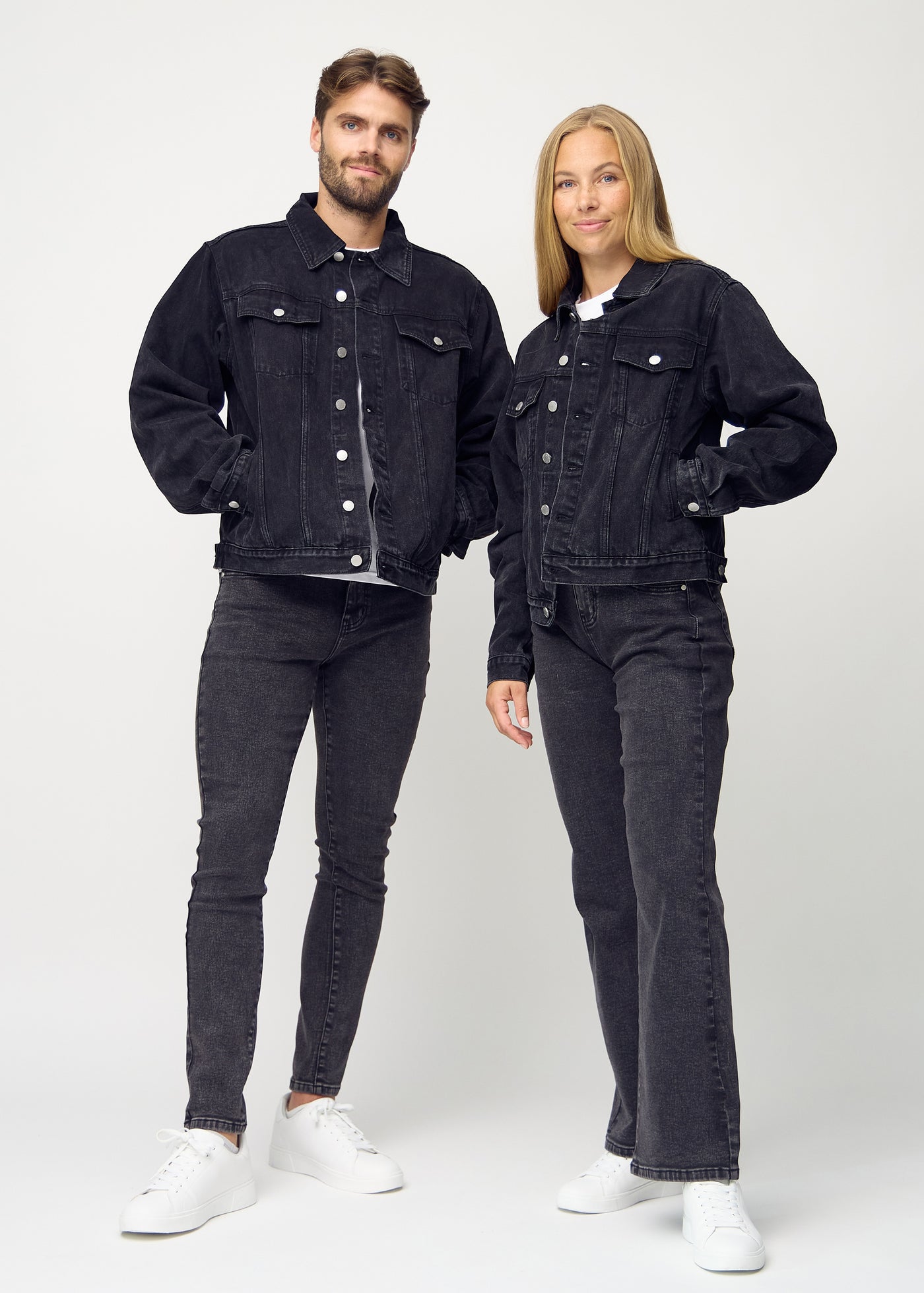 Fuldt billede af unisex mørkegrå denim jakke, set forfra på herre og dame model, med knapper og lommeplacering tydeligt synlige.