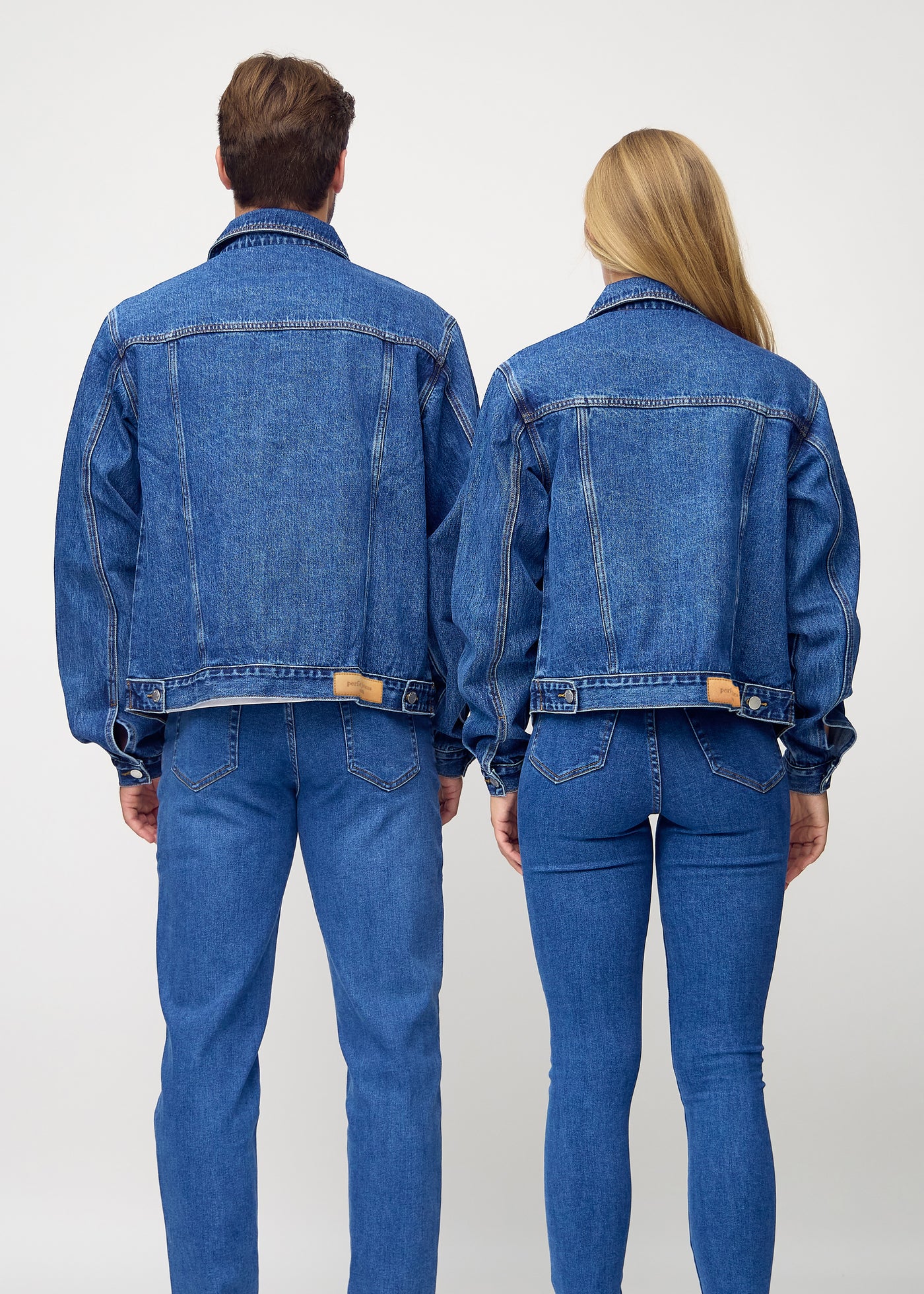 Unisex mørkeblå denim jakke set bagfra på mand og kvinde, viser rygdetaljer og højkvalitetssømme.
