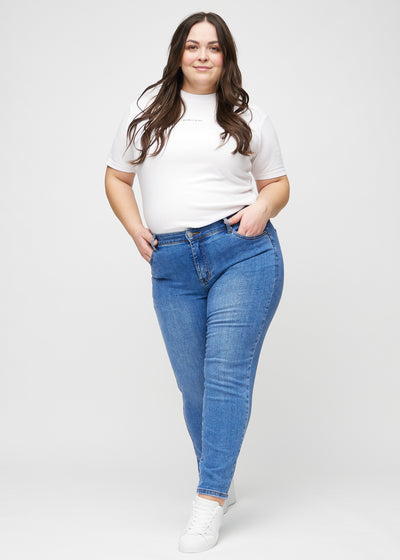 Plus-size model går ind i billedet, strækker i sine jeans, viser dem frem ved at dreje rundt, og forlader derefter billedet.